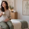 Woman in a bright Manhattan wellness room resting a hand on her lower abdomen, illustrating hormonal bloating vs water retention